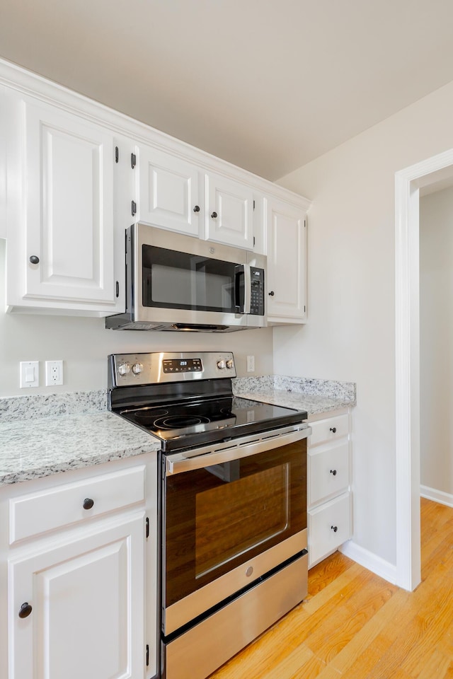 kitchen with light stone counters, appliances with stainless steel finishes, white cabinetry, light wood-type flooring, and baseboards