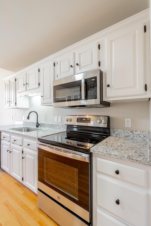 kitchen featuring white cabinets, light wood-style floors, stainless steel appliances, and a sink