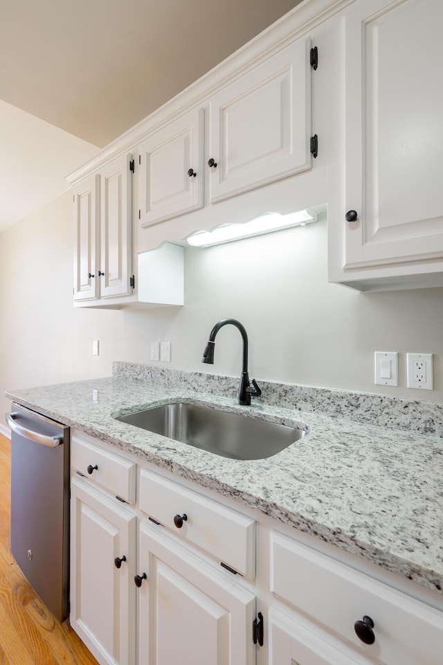 kitchen with a sink, light stone countertops, white cabinets, and dishwasher