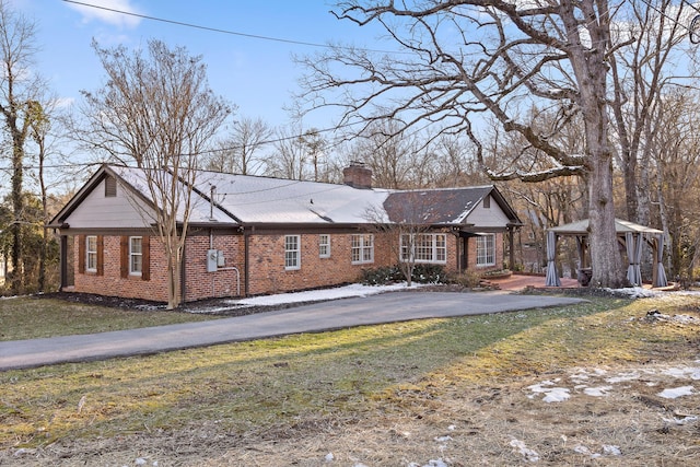 single story home featuring driveway, brick siding, a chimney, a gazebo, and a front yard