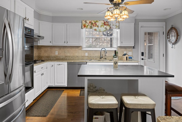 kitchen with a breakfast bar area, stainless steel appliances, a sink, white cabinetry, and crown molding