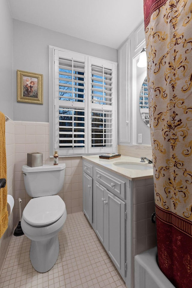 bathroom with toilet, tile patterned flooring, tile walls, and wainscoting