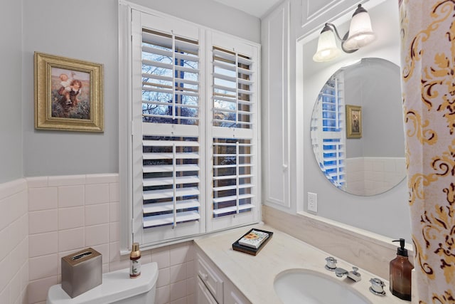 bathroom featuring wainscoting, tile walls, toilet, and vanity