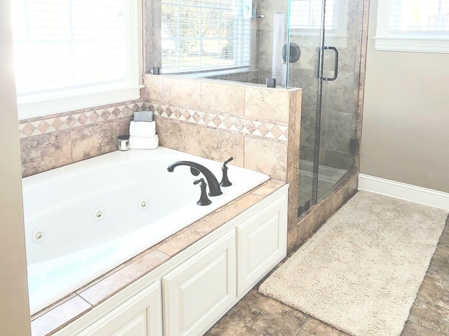 full bathroom with a jetted tub, a shower stall, baseboards, and stone finish flooring