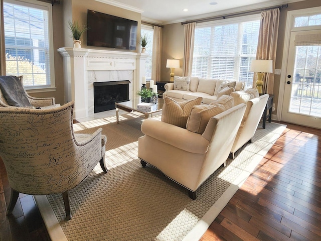 living area with plenty of natural light, wood finished floors, a high end fireplace, and crown molding