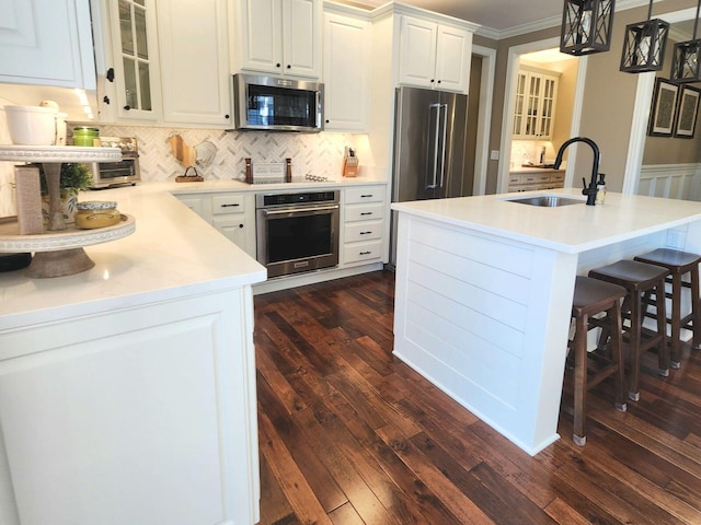 kitchen featuring pendant lighting, stainless steel appliances, light countertops, white cabinets, and a sink