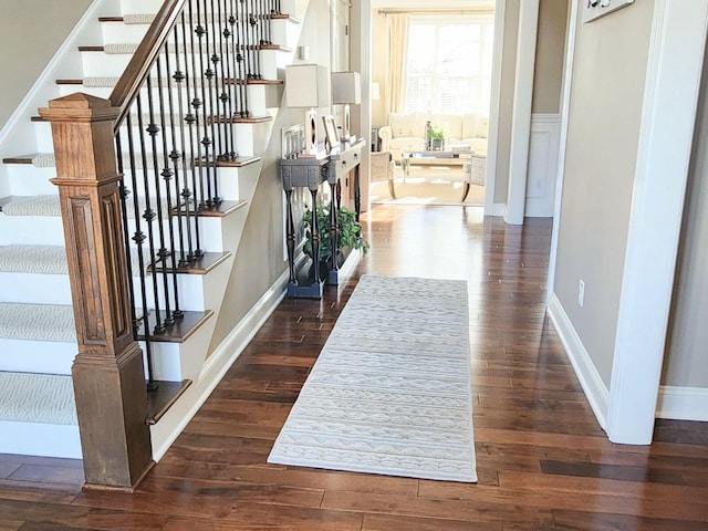 hallway with stairs, dark wood-style flooring, and baseboards