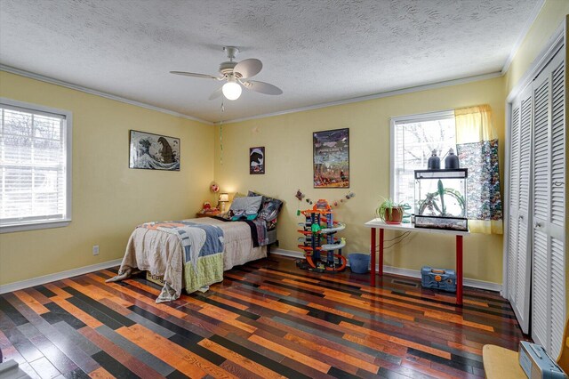 bedroom with dark wood-style floors, crown molding, a closet, ceiling fan, and baseboards