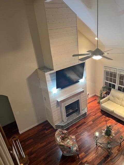 living room with dark wood-type flooring, ceiling fan, high vaulted ceiling, a tile fireplace, and baseboards