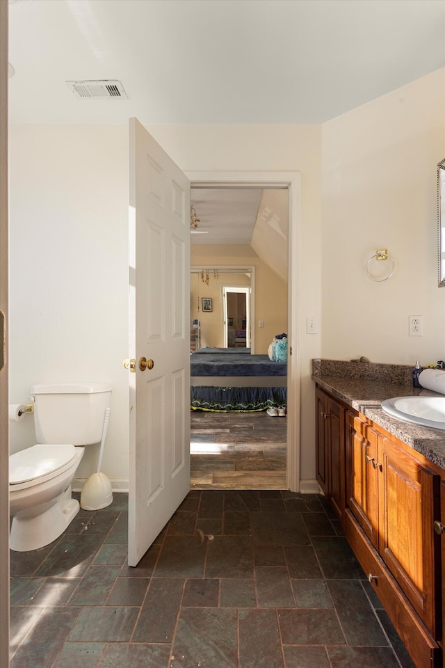 bathroom featuring toilet, vanity, visible vents, stone finish flooring, and ensuite bath