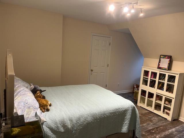 bedroom featuring vaulted ceiling, track lighting, dark wood finished floors, and baseboards