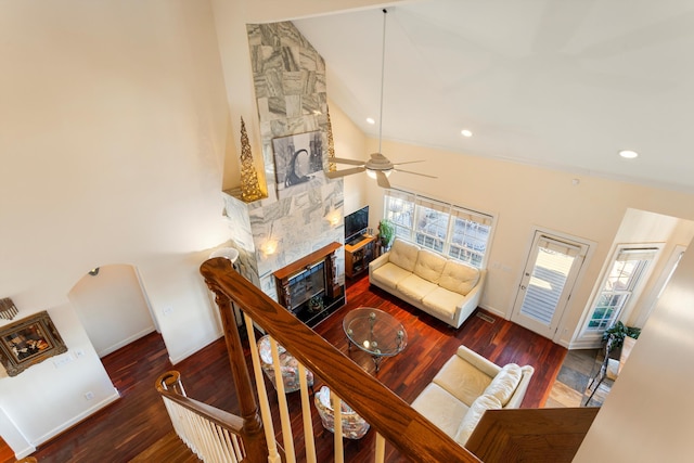 living room featuring dark wood-type flooring, high vaulted ceiling, a stone fireplace, and baseboards