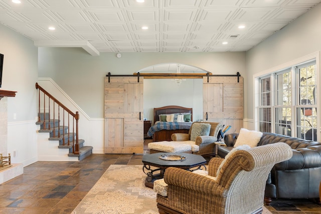 living room featuring a barn door, visible vents, stone finish flooring, stairs, and recessed lighting