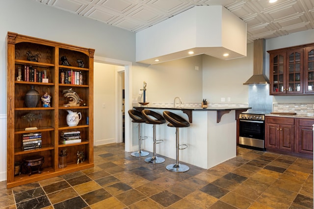 kitchen featuring electric stove, an ornate ceiling, glass insert cabinets, a kitchen breakfast bar, and extractor fan