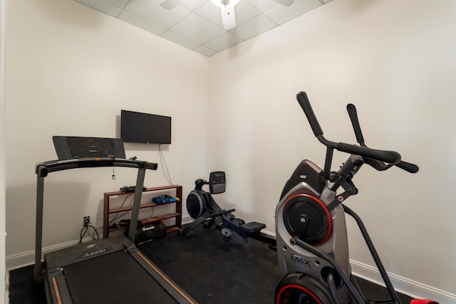 workout area featuring a ceiling fan, a paneled ceiling, and baseboards