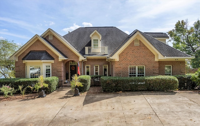 view of front of house featuring brick siding, roof with shingles, a gate, and a balcony