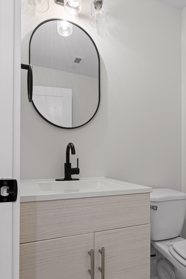 bathroom with toilet, vanity, and visible vents