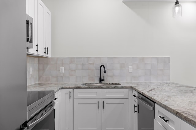 kitchen with light stone countertops, stainless steel appliances, a sink, white cabinets, and decorative backsplash