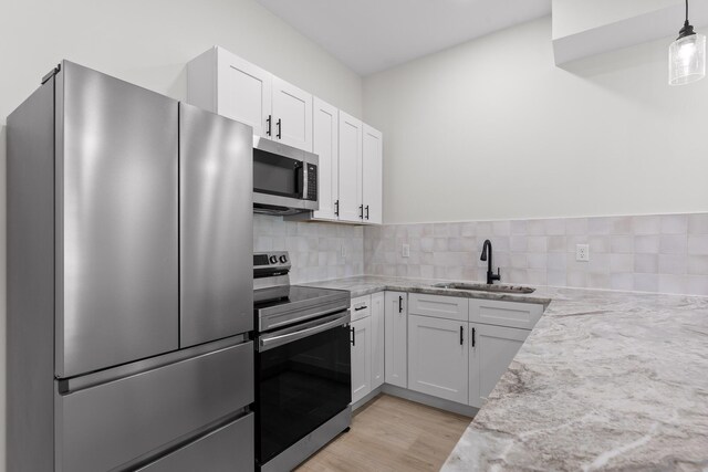 kitchen featuring white cabinets, appliances with stainless steel finishes, light stone countertops, pendant lighting, and a sink