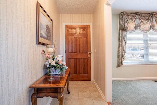 doorway featuring light tile patterned floors, a textured ceiling, baseboards, and wallpapered walls