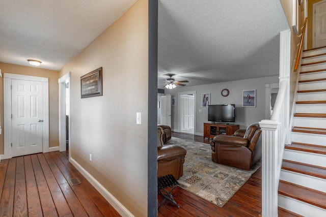 living area featuring a textured ceiling, wood finished floors, a ceiling fan, baseboards, and stairs