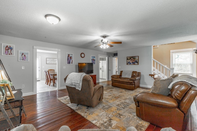 living room featuring a textured ceiling, wood finished floors, a ceiling fan, baseboards, and stairway