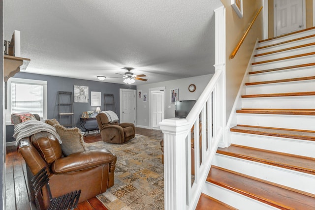 living room with a ceiling fan, a textured ceiling, wood finished floors, baseboards, and stairs