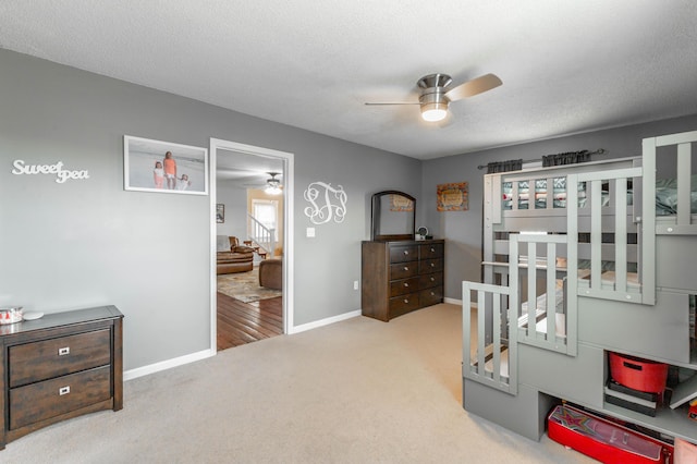 bedroom featuring a ceiling fan, light carpet, a textured ceiling, and baseboards