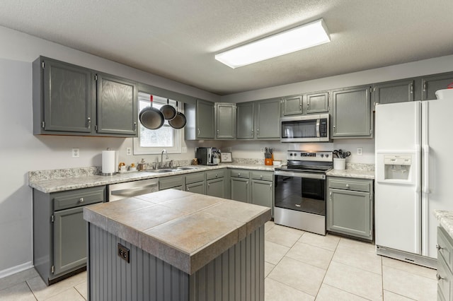 kitchen featuring appliances with stainless steel finishes, a center island, light countertops, gray cabinets, and a sink