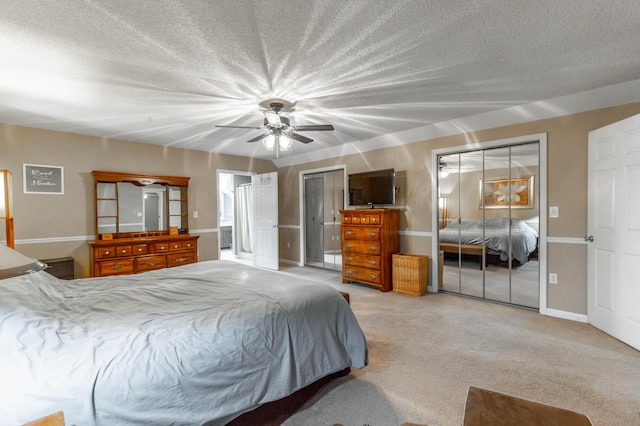 bedroom featuring a textured ceiling, light colored carpet, a ceiling fan, multiple closets, and baseboards