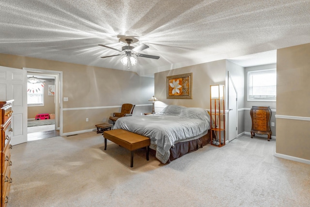 bedroom featuring a ceiling fan, light carpet, a textured ceiling, and baseboards