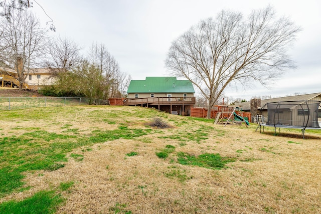 view of yard with a fenced backyard, a trampoline, a deck, and a playground