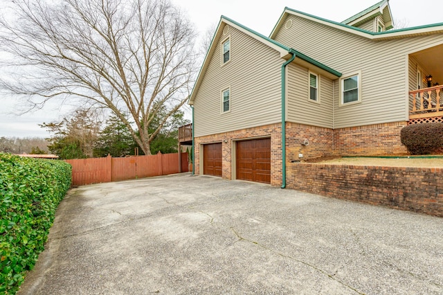 view of home's exterior with an attached garage, driveway, fence, and brick siding