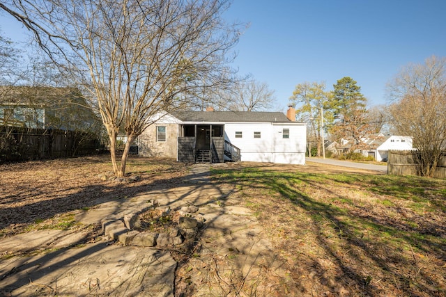 rear view of house featuring entry steps, fence, and a chimney