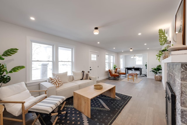 living area with baseboards, a stone fireplace, light wood-style flooring, and recessed lighting