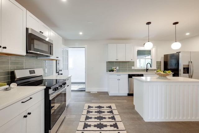 kitchen featuring decorative light fixtures, light countertops, appliances with stainless steel finishes, white cabinetry, and a sink