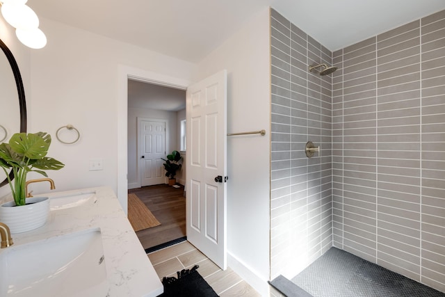 full bathroom featuring double vanity, wood tiled floor, a tile shower, and a sink