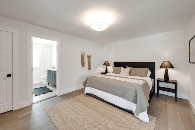 bedroom with baseboards, wood finished floors, and ensuite bathroom