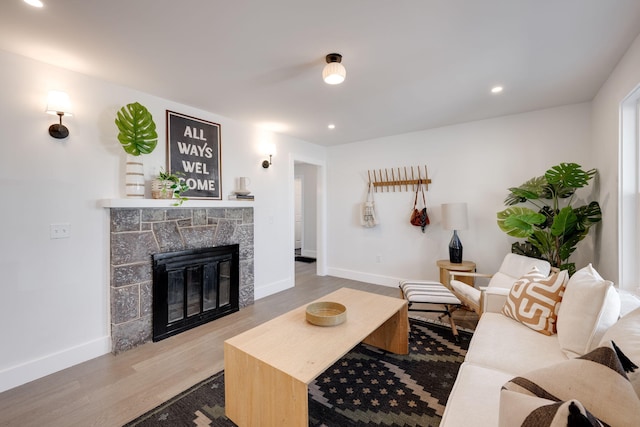 living area featuring a stone fireplace, recessed lighting, wood finished floors, and baseboards