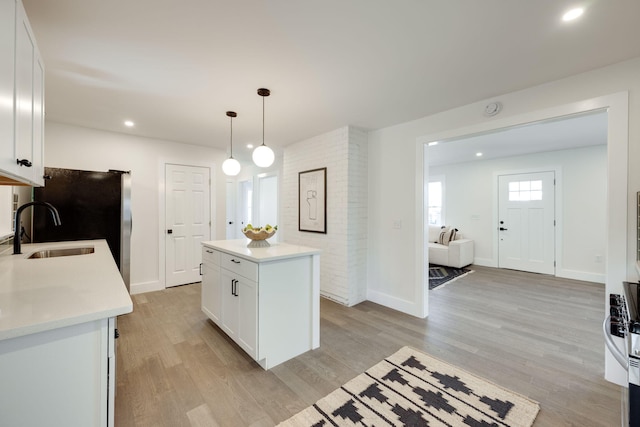 kitchen featuring light countertops, hanging light fixtures, white cabinets, a kitchen island, and a sink