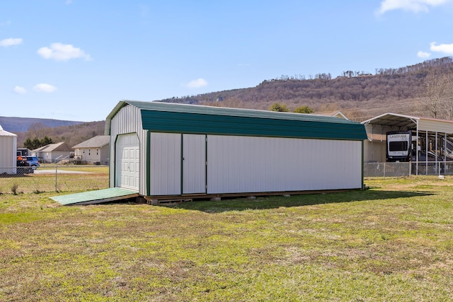 view of outdoor structure with a carport, an outbuilding, fence, and a mountain view