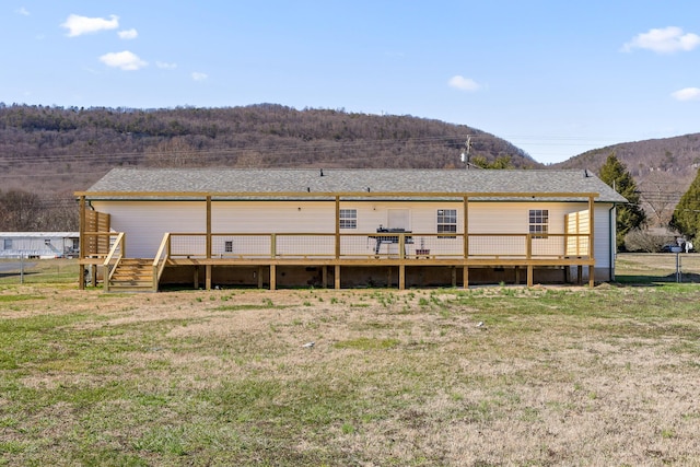 rear view of house featuring fence, a wooden deck, and a lawn