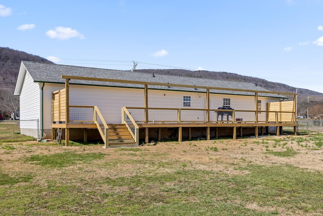 rear view of property featuring a shingled roof, fence, and a wooden deck