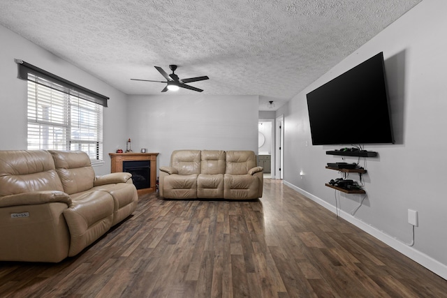 living room with ceiling fan, a textured ceiling, dark wood-style flooring, a fireplace, and baseboards