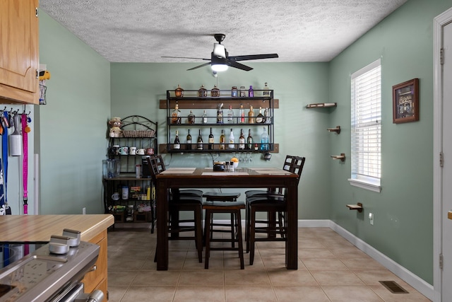 dining room featuring light tile patterned floors, visible vents, baseboards, ceiling fan, and a textured ceiling