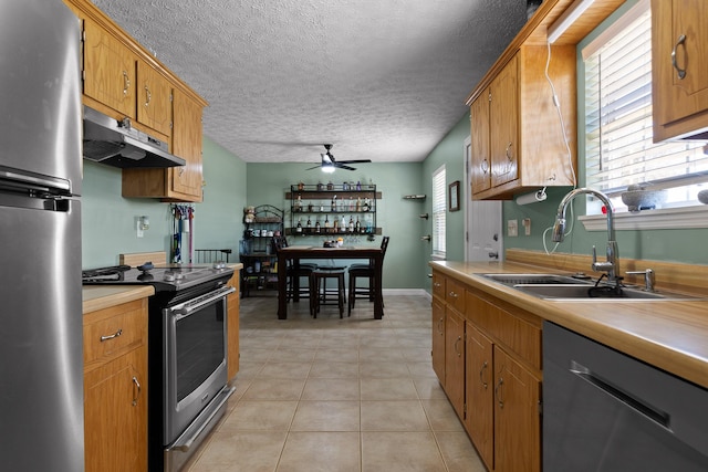 kitchen with light tile patterned floors, light countertops, appliances with stainless steel finishes, a sink, and under cabinet range hood