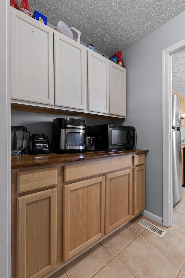 kitchen with black microwave, a textured ceiling, light tile patterned flooring, visible vents, and freestanding refrigerator