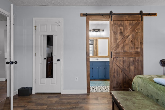 bedroom featuring a textured ceiling, a barn door, a sink, baseboards, and dark wood-style floors