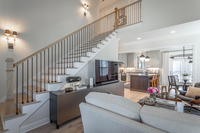 living area with stairway, a towering ceiling, and light wood-style flooring