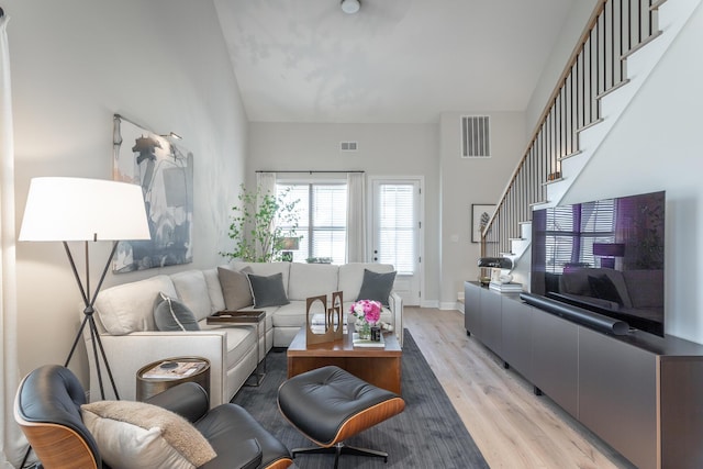 living room featuring light wood-type flooring, stairway, baseboards, and visible vents